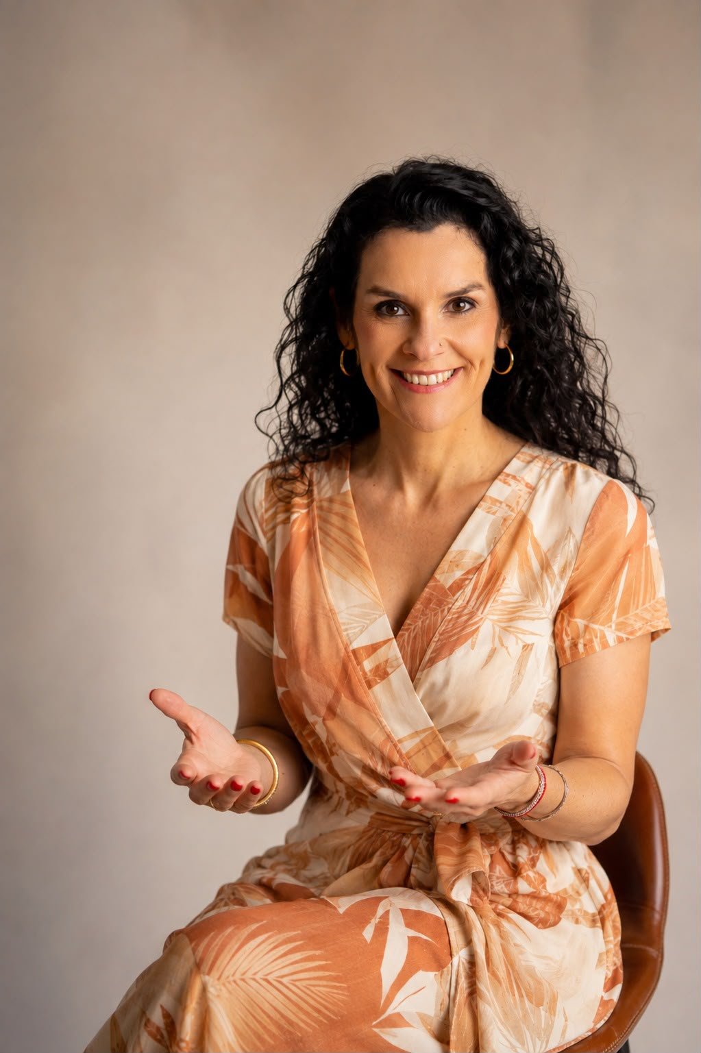 Lu Rodrigues sorrindo, sentada e com as mãos abertas